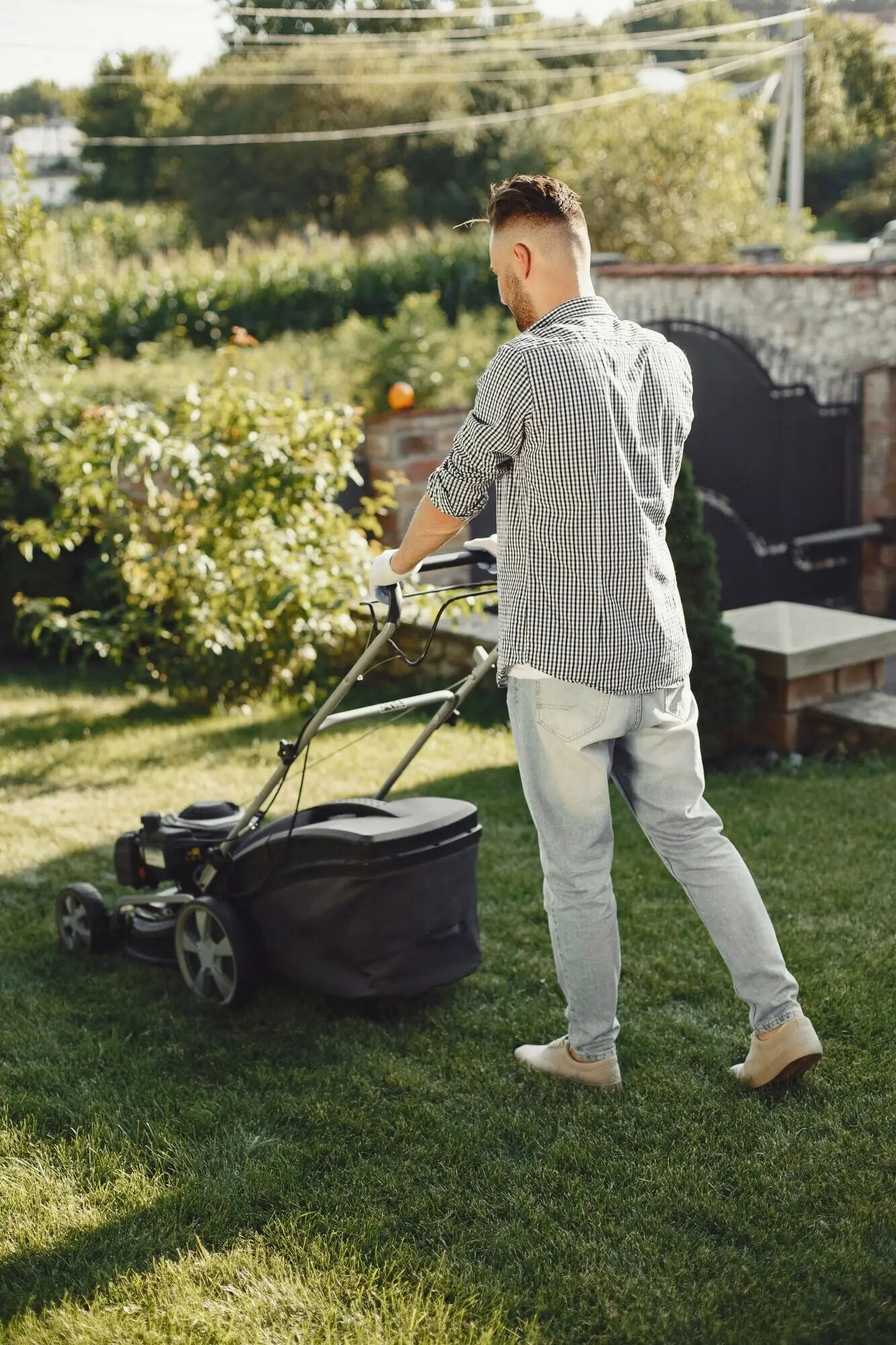 A man wearing a shirt is mowing the grass in the backyard with a lawn mower.